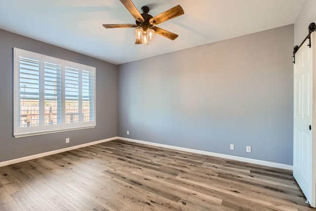 unfurnished room featuring wood-type flooring, a barn door, and ceiling fan