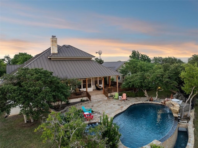 pool at dusk with pool water feature, a patio area, and a deck