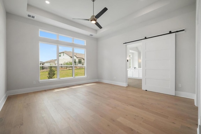 917 Bristol Creek Bnd, Lakeway, TX 78738 - unfurnished bedroom featuring a tray ceiling, a barn door, light wood-style floors, recessed lighting, and ensuite bath