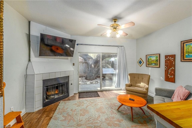 living room with ceiling fan, wood-type flooring, and a tile fireplace