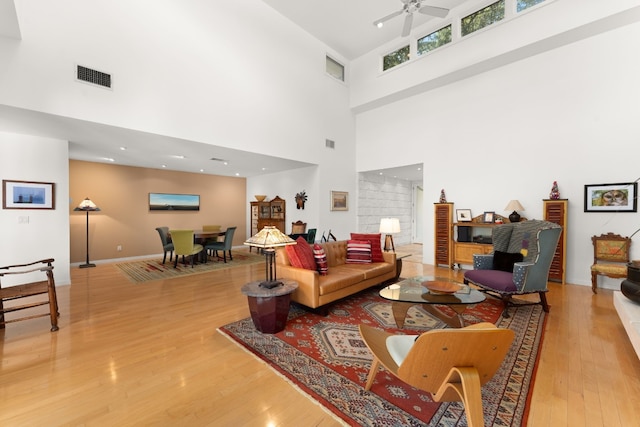 living room featuring ceiling fan, hardwood / wood-style floors, and a towering ceiling