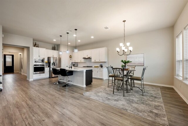 kitchen with white cabinets, appliances with stainless steel finishes, a center island with sink, and pendant lighting