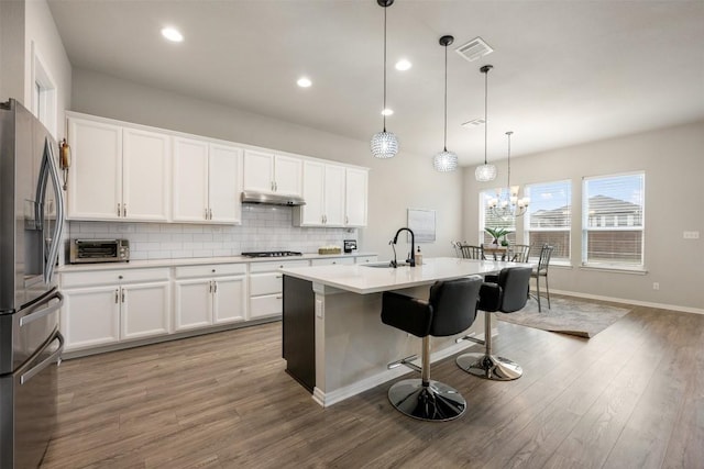 kitchen with gas cooktop, stainless steel refrigerator with ice dispenser, a kitchen island with sink, pendant lighting, and white cabinets