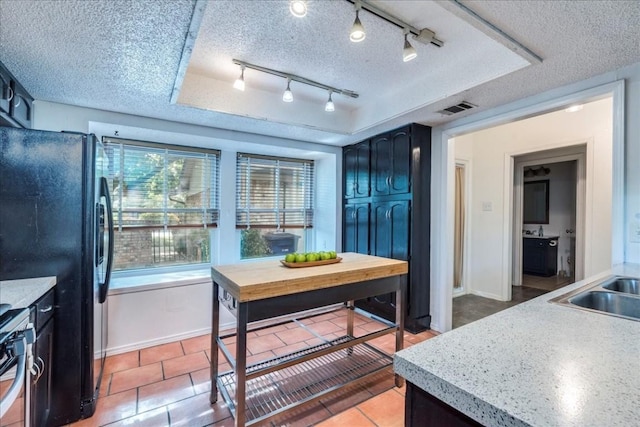 kitchen featuring black fridge, a textured ceiling, a raised ceiling, sink, and tile patterned flooring