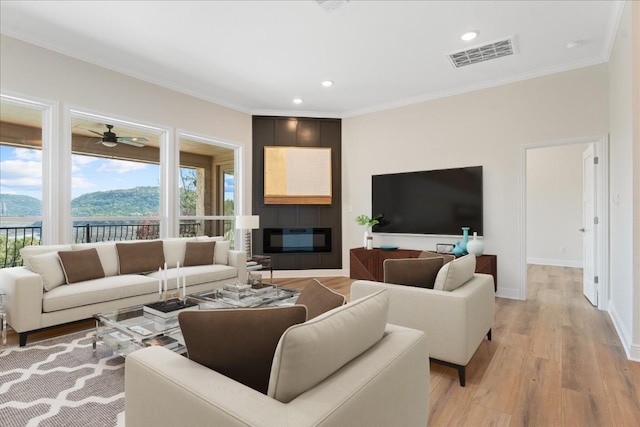 living room with a fireplace, a mountain view, light wood-type flooring, ceiling fan, and crown molding