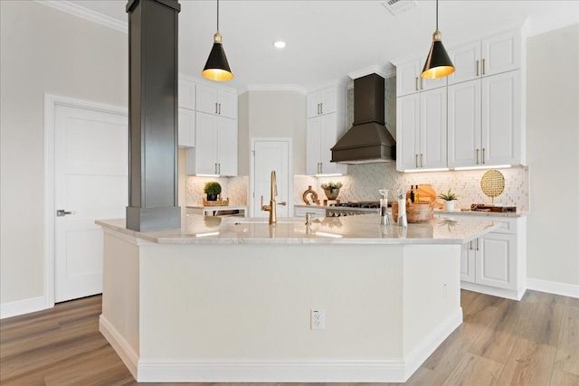 kitchen featuring custom range hood, white cabinetry, pendant lighting, and a center island with sink