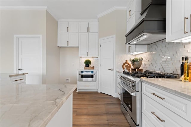 kitchen featuring white cabinets, custom range hood, appliances with stainless steel finishes, light stone countertops, and crown molding