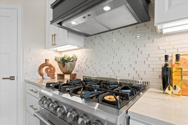 room details with high end range, white cabinets, backsplash, and custom range hood