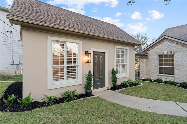 view of front facade featuring a shingled roof, a front yard, and stucco siding