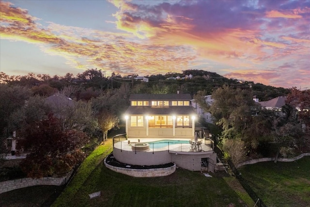 back of house at dusk with an outdoor pool, a lawn, and a patio