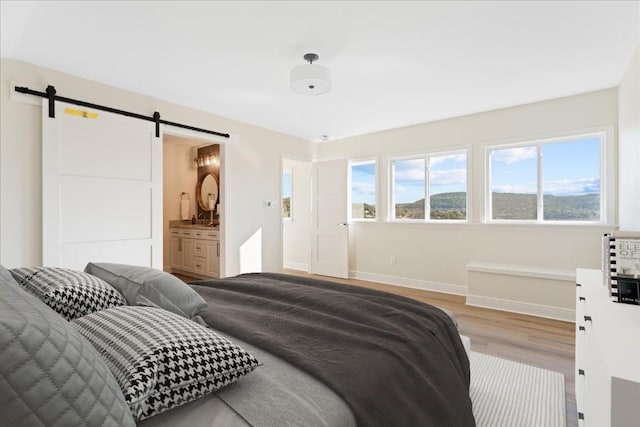 bedroom with multiple windows, light hardwood / wood-style floors, a barn door, and ensuite bath