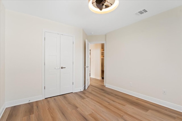 unfurnished bedroom featuring light wood-style flooring, a closet, visible vents, and baseboards