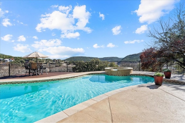 view of swimming pool featuring a pool with connected hot tub, a mountain view, a patio, and fence