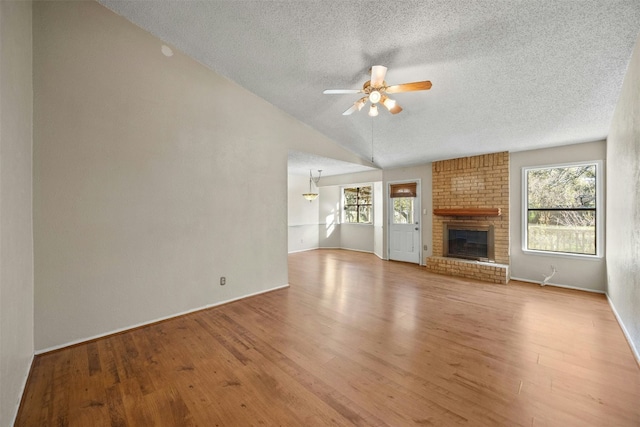 unfurnished living room featuring plenty of natural light, ceiling fan, lofted ceiling, and a brick fireplace