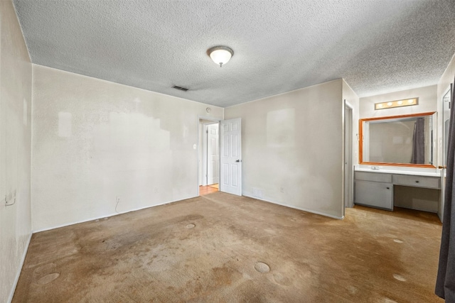 unfurnished bedroom with carpet flooring, connected bathroom, and a textured ceiling