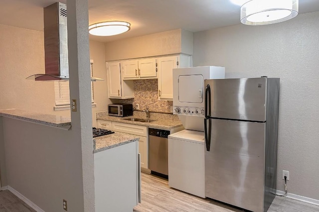 kitchen with appliances with stainless steel finishes, ventilation hood, sink, stacked washer and dryer, and white cabinetry