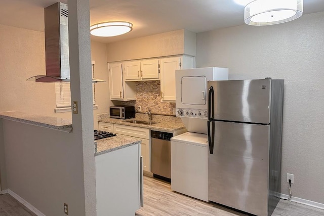 2401 Manor Rd Unit 236, Austin, TX 78722 - kitchen featuring appliances with stainless steel finishes, island exhaust hood, a sink, stacked washing machine and dryer, and light wood-style flooring