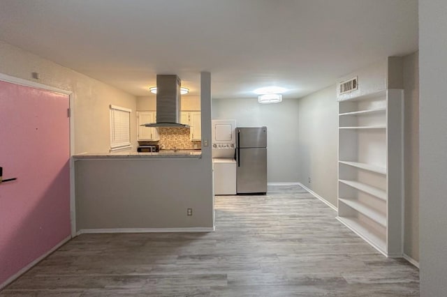 2401 Manor Rd Unit 236, Austin, TX 78722 - kitchen with freestanding refrigerator, island range hood, light wood finished floors, and a peninsula