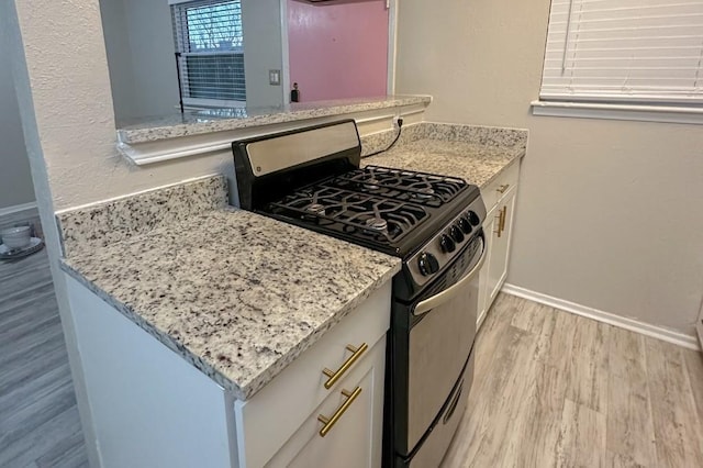 2401 Manor Rd Unit 236, Austin, TX 78722 - kitchen featuring stainless steel gas range, light wood finished floors, light stone counters, baseboards, and white cabinetry