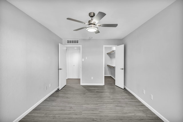 unfurnished bedroom featuring a spacious closet, a closet, ceiling fan, and dark hardwood / wood-style floors