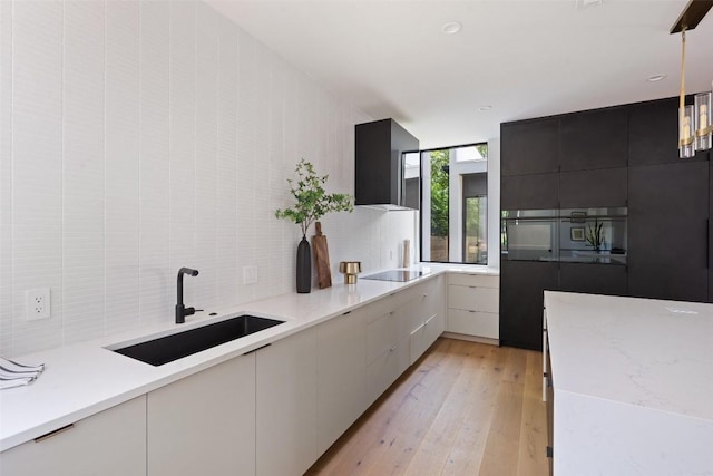 kitchen with exhaust hood, sink, light hardwood / wood-style floors, light stone counters, and white cabinetry