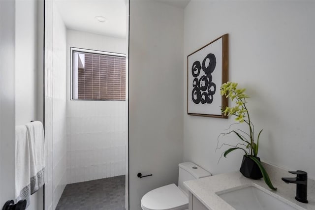 bathroom featuring tiled shower, vanity, and toilet