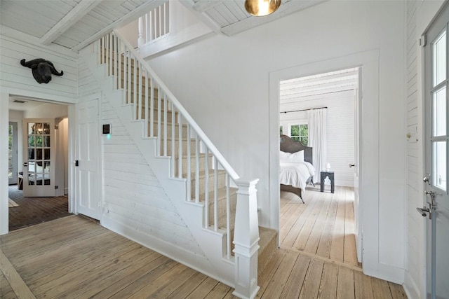 staircase with beamed ceiling, wood walls, and wood-type flooring