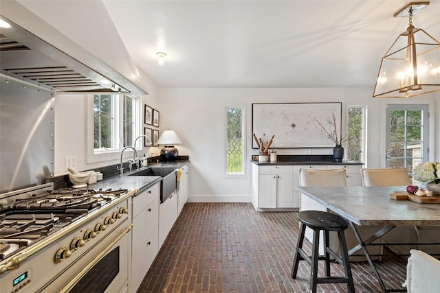 kitchen featuring stainless steel range, extractor fan, sink, white cabinetry, and hanging light fixtures