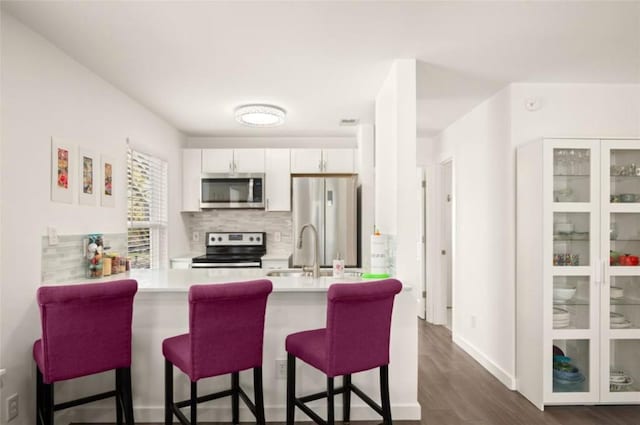 kitchen with kitchen peninsula, appliances with stainless steel finishes, backsplash, a kitchen breakfast bar, and white cabinets