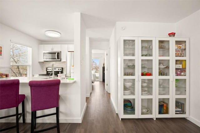 kitchen with dark hardwood / wood-style floors, backsplash, a kitchen bar, white cabinets, and appliances with stainless steel finishes