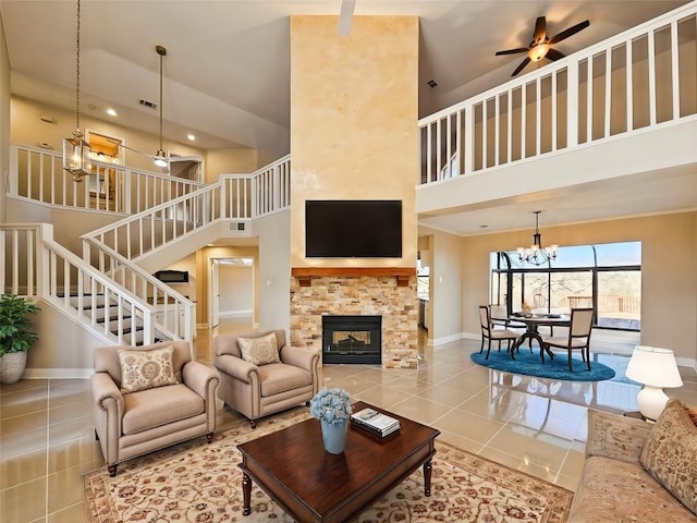 living room with a stone fireplace, tile patterned flooring, a towering ceiling, and ceiling fan with notable chandelier