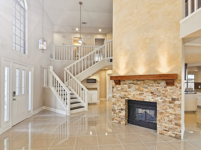 foyer entrance featuring a stone fireplace, light tile patterned flooring, and a towering ceiling