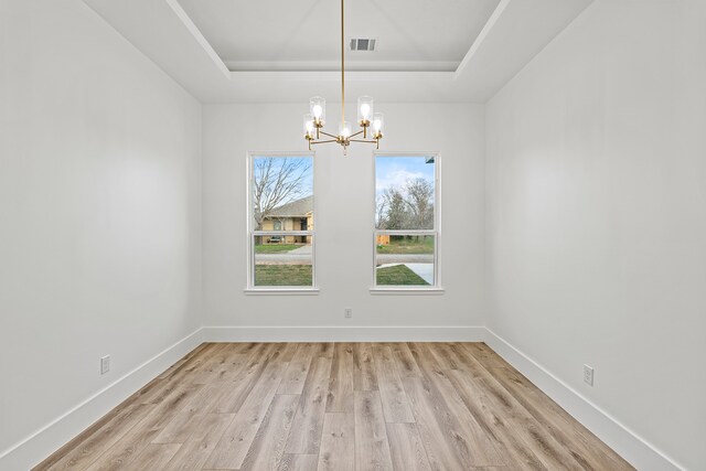 unfurnished room featuring a raised ceiling, light wood-type flooring, and a notable chandelier