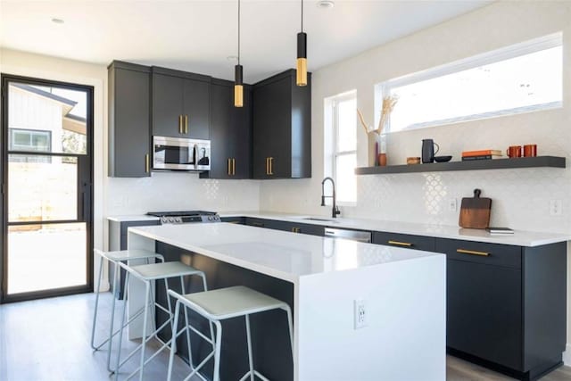 kitchen with sink, hanging light fixtures, a kitchen bar, a kitchen island, and appliances with stainless steel finishes