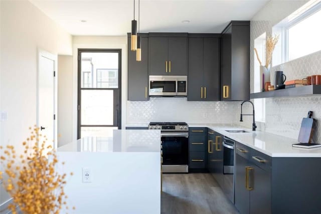 kitchen with appliances with stainless steel finishes, backsplash, sink, hardwood / wood-style floors, and hanging light fixtures