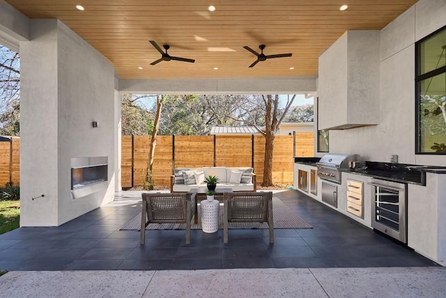 view of patio / terrace with area for grilling, ceiling fan, an outdoor living space with a fireplace, wine cooler, and a grill