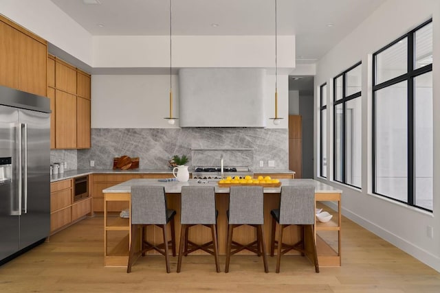 kitchen featuring pendant lighting, built in appliances, a kitchen island, and wall chimney exhaust hood