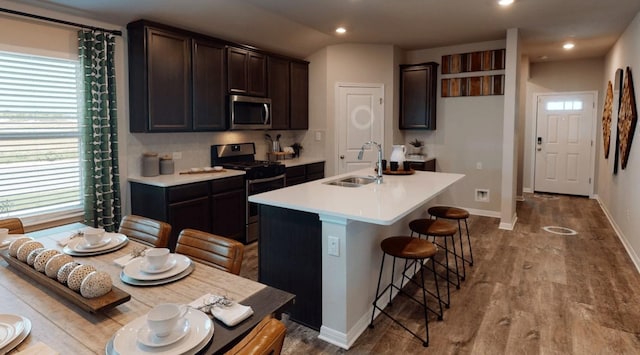 kitchen with a kitchen island with sink, a kitchen breakfast bar, sink, appliances with stainless steel finishes, and light hardwood / wood-style floors