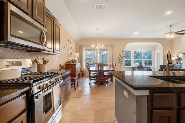 kitchen featuring sink, dark stone countertops, ceiling fan with notable chandelier, hanging light fixtures, and appliances with stainless steel finishes