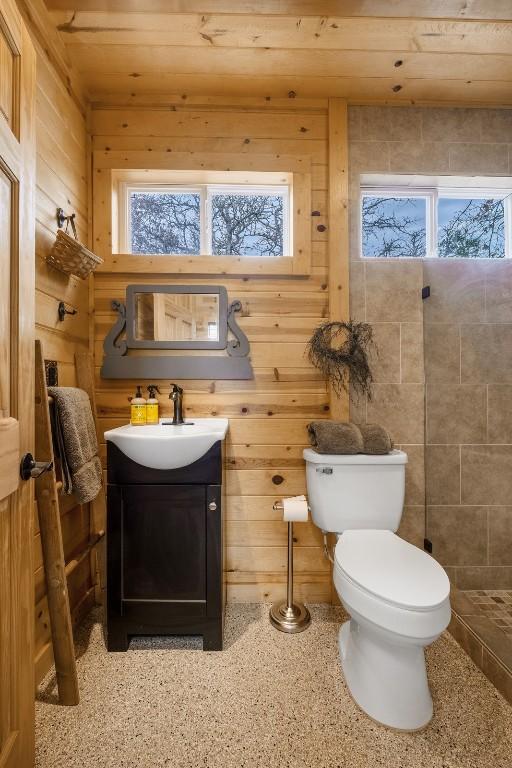 bathroom featuring speckled floor, toilet, wood walls, and vanity