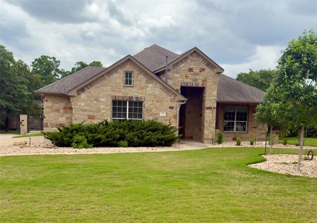 view of front of property featuring stone siding, a front yard, and a shingled roof