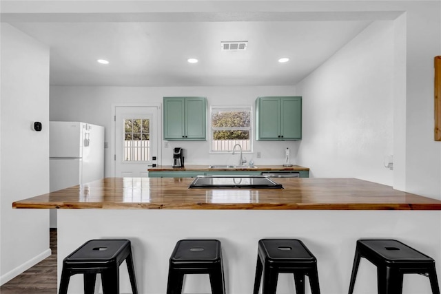 kitchen featuring green cabinetry, a breakfast bar area, and wooden counters