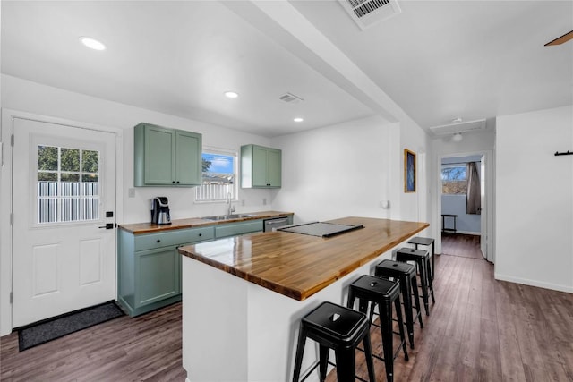 kitchen featuring a breakfast bar area, green cabinets, sink, and wood counters