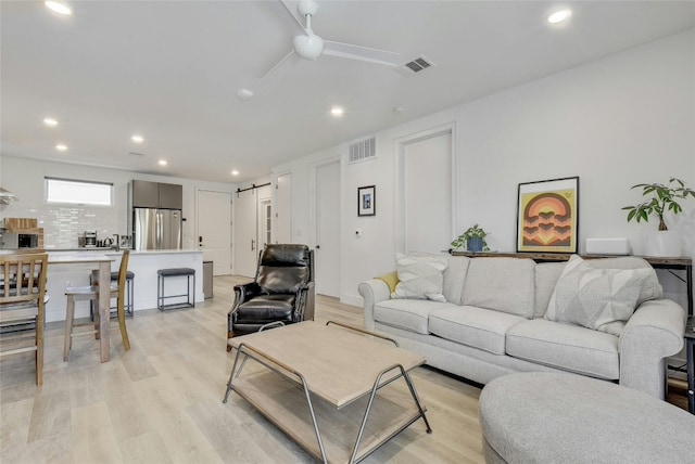 living room with light wood-type flooring, ceiling fan, and a barn door