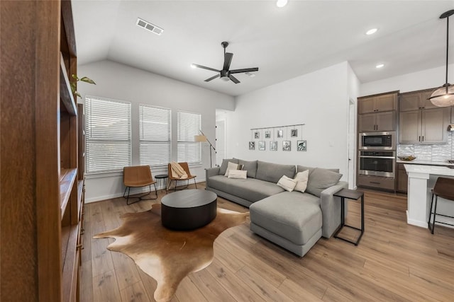 living room with ceiling fan, vaulted ceiling, and light wood-type flooring