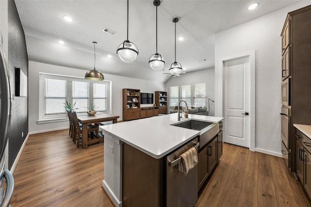 kitchen with sink, hanging light fixtures, stainless steel appliances, an island with sink, and dark brown cabinets