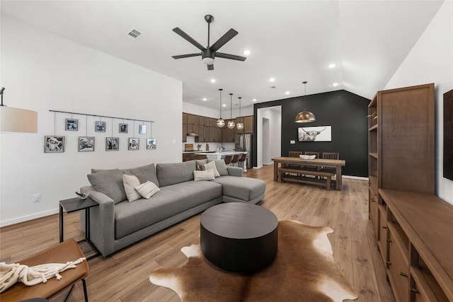 living room with ceiling fan, light hardwood / wood-style floors, sink, and vaulted ceiling