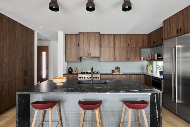 kitchen featuring sink, stainless steel built in fridge, a kitchen bar, and an island with sink