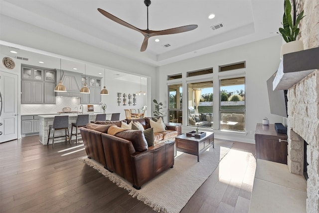 living room featuring ceiling fan, dark hardwood / wood-style floors, a raised ceiling, and a fireplace