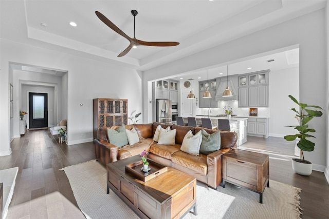 living room with a tray ceiling, ceiling fan, sink, and hardwood / wood-style flooring